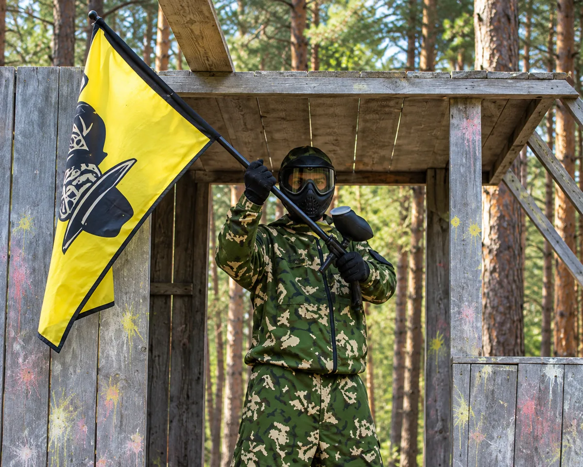 Участник пейнтбола с жёлтым флагом в игровом домике
